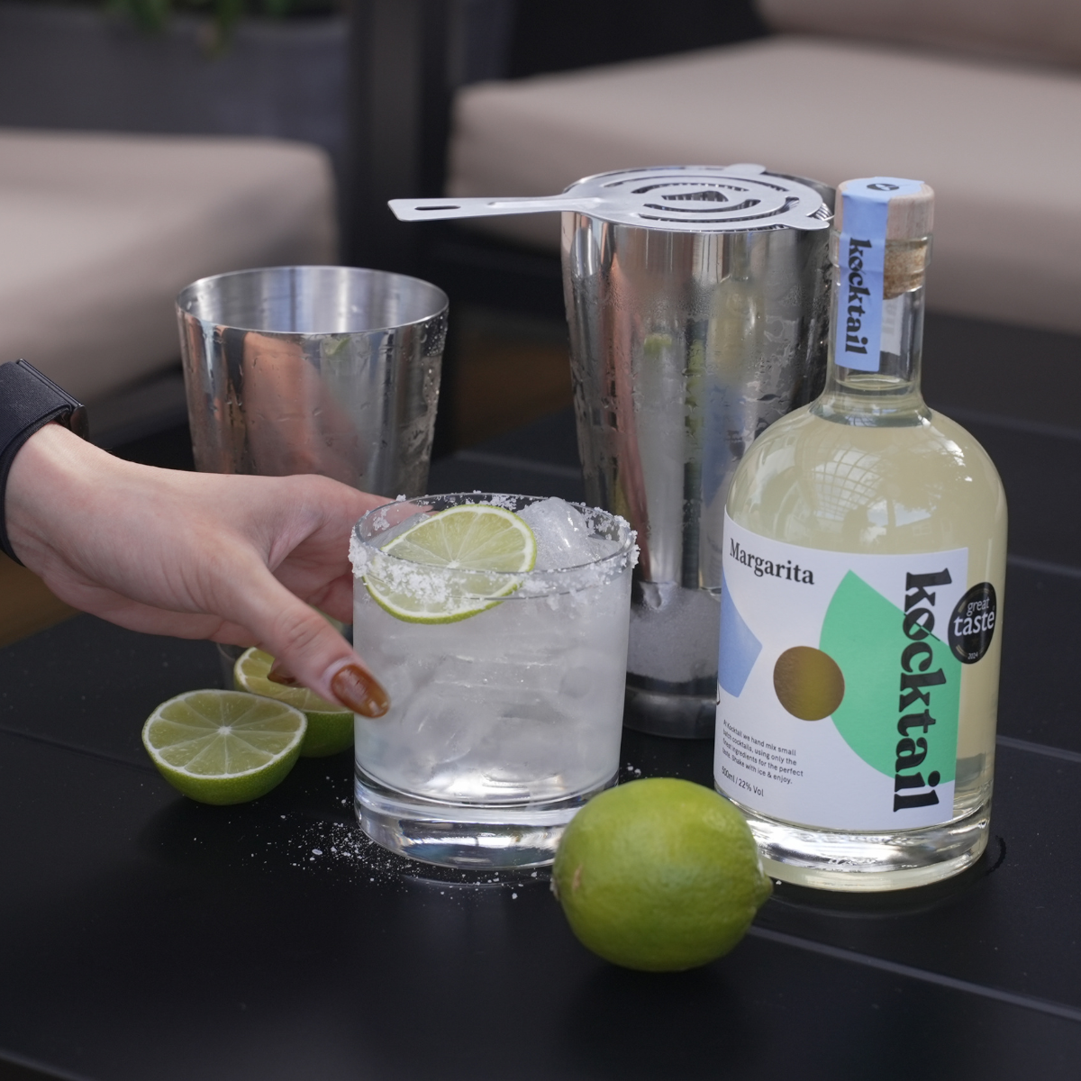 Margarita glass with lime garnish next to a bottle of Margarita cocktail on a table.