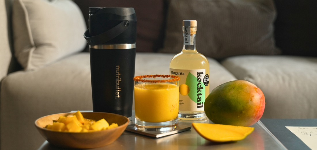 Bottle of Kocktail Margarita next to a blender filled with frozen mango cocktail mix