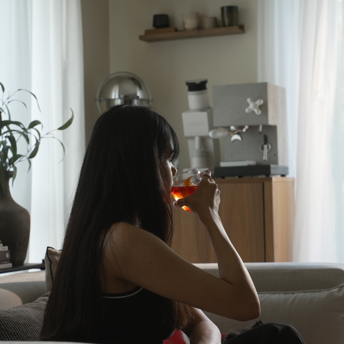 Woman sitting on a couch drinking a negroni in a cozy living room.
